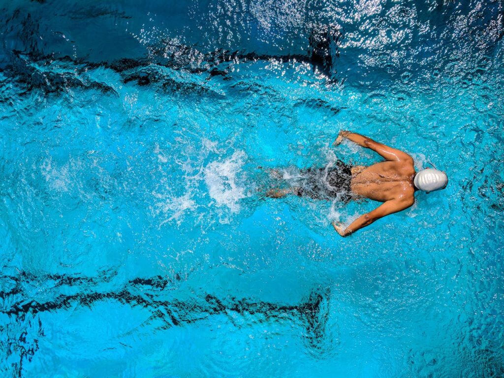 pexels photo 863988 Top view of a swimmer wearing a cap, performing a front crawl stroke in a clear blue swimming pool.